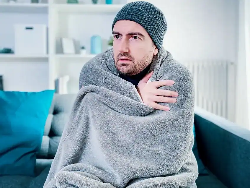Frierender Mann in eine Decke gehüllt neben dem kalten Heizkörper